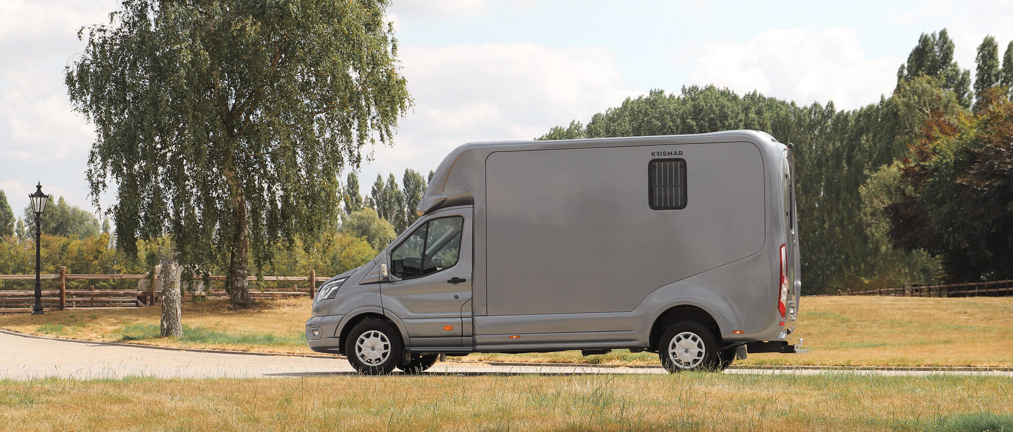 Zijaanzicht van een grijze 2 paards wagen van het merk Krismar Horse Trucks.