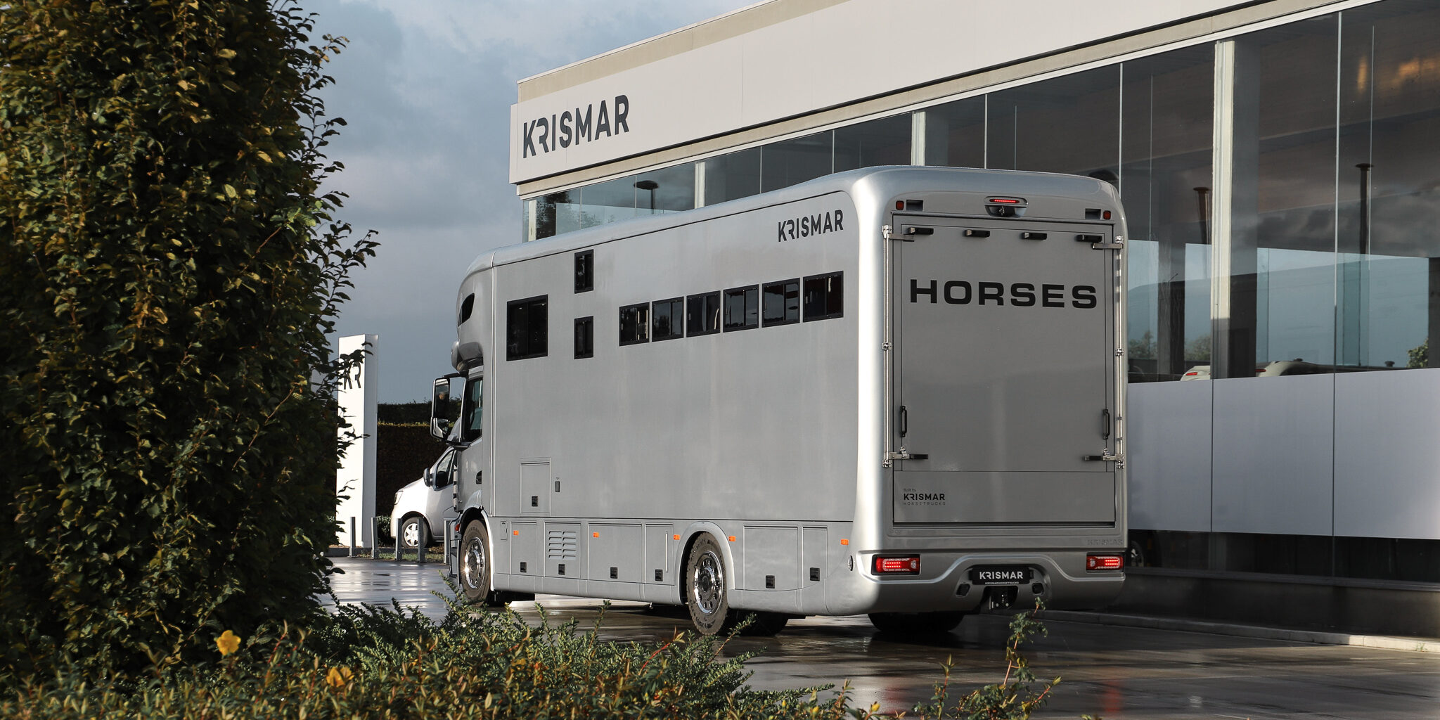 De achterkant van een lichtgrijze Krismar paardenvrachtwagen met de laadklep gesloten.