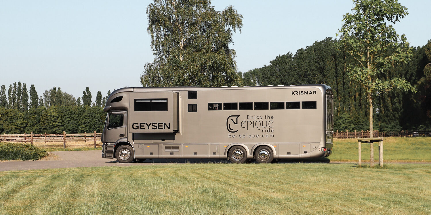 The side of a grey Krismar horse truck with pop-out open and logo from the client on.