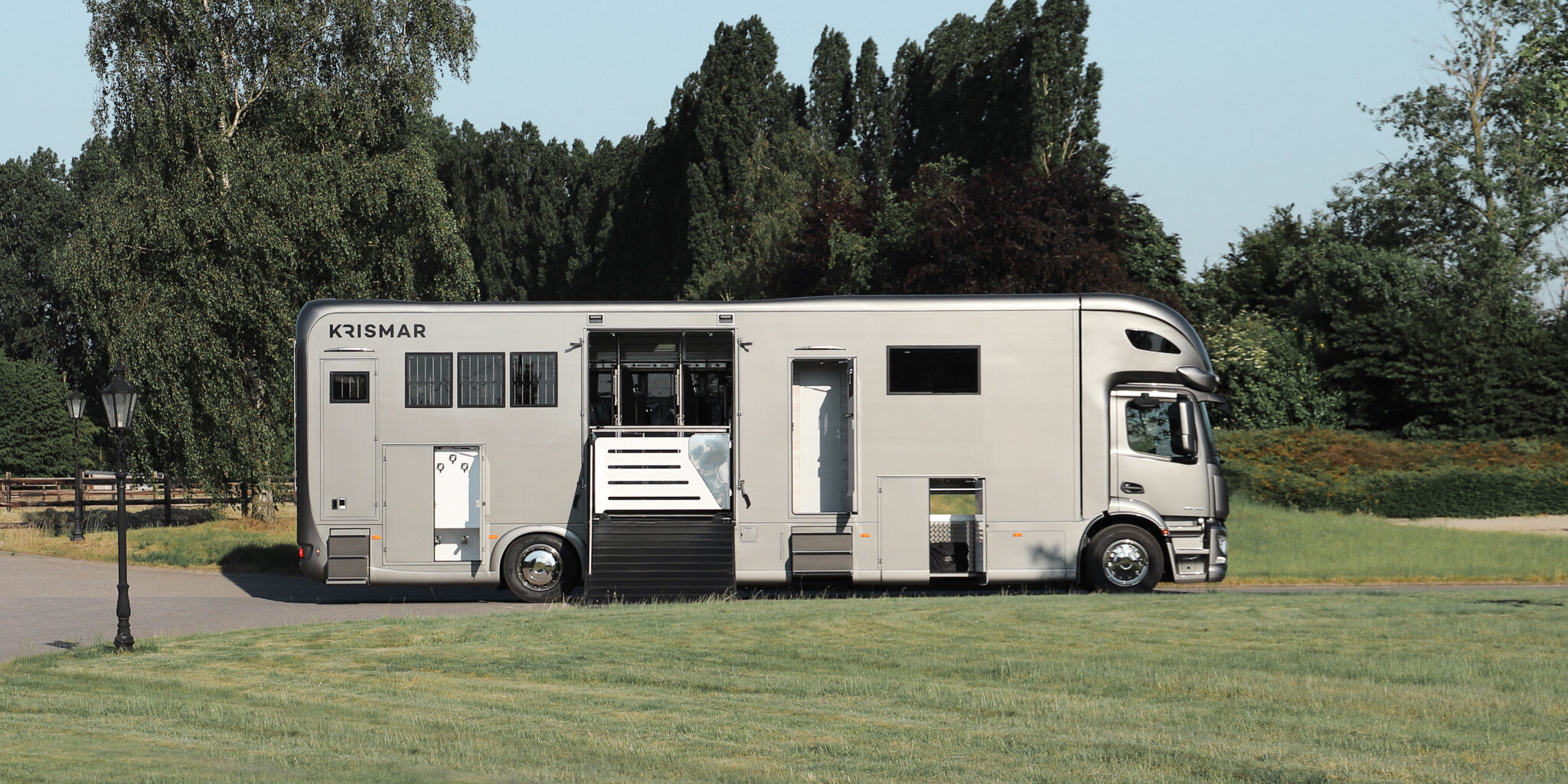 The side of a grey Krismar horse truck with all doors and loading ramp open.