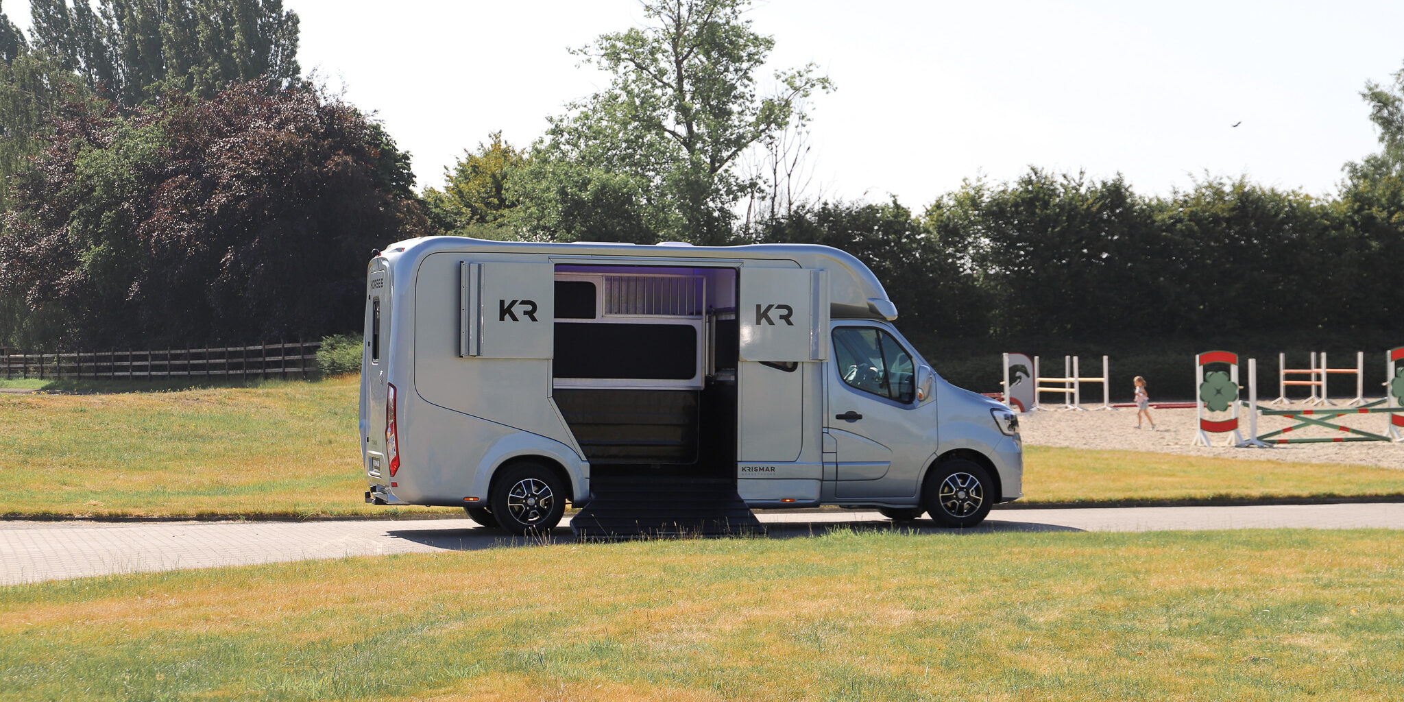 A light grey 2-horse camionette with the loading ramp on the side open.