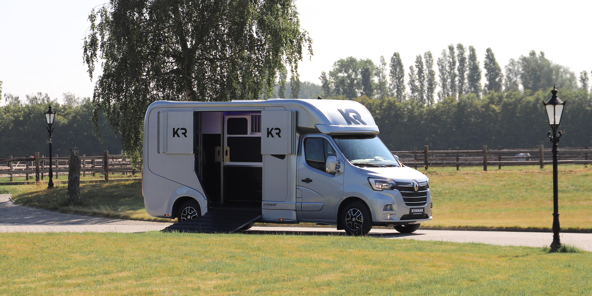 A light grey Krismar 2-horse camionette with the loading ramp on the side open.