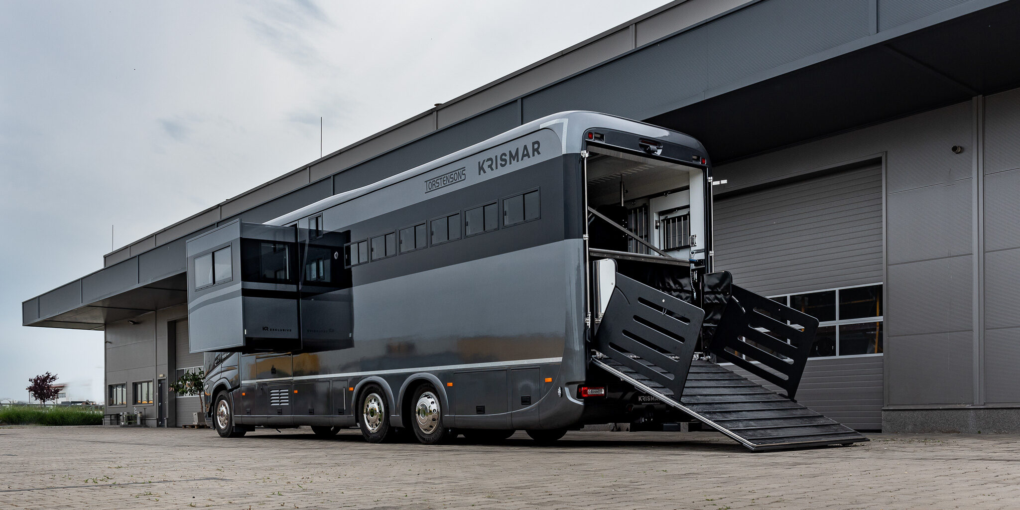 Een grijze Krismar paardenvrachtwagen met de laadklep en de pop-out geopend.